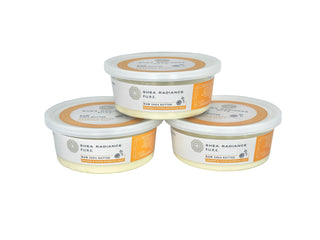 Three containers of orange & clove small Shea Radiance raw shea butter on a white background