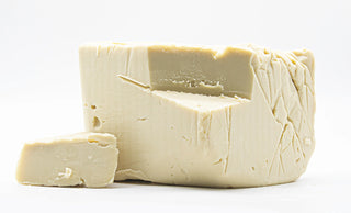 Block of white cheese with a slice cut off on a white background