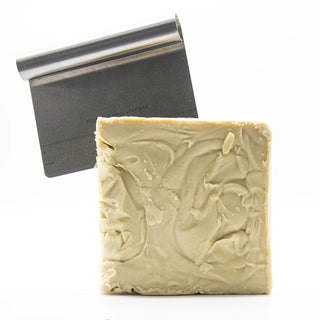 Bar of soap with a decorative design next to a metal soap dish on a white background